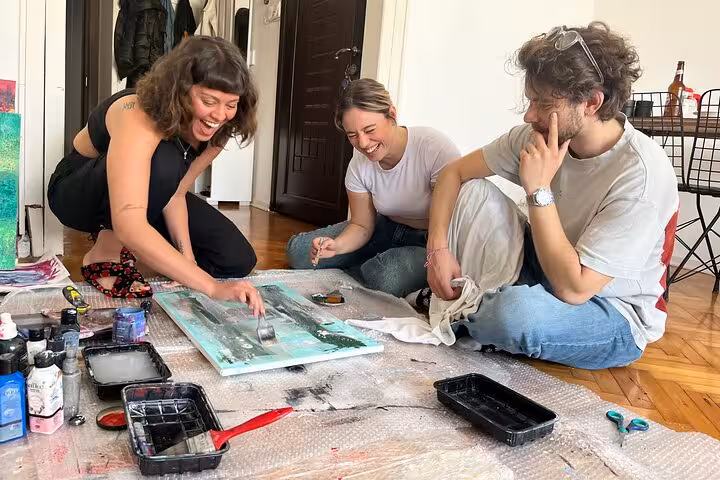 Friends laugh during Istanbul wine and paint session at a local home, guided art escape with canvas and drinks
