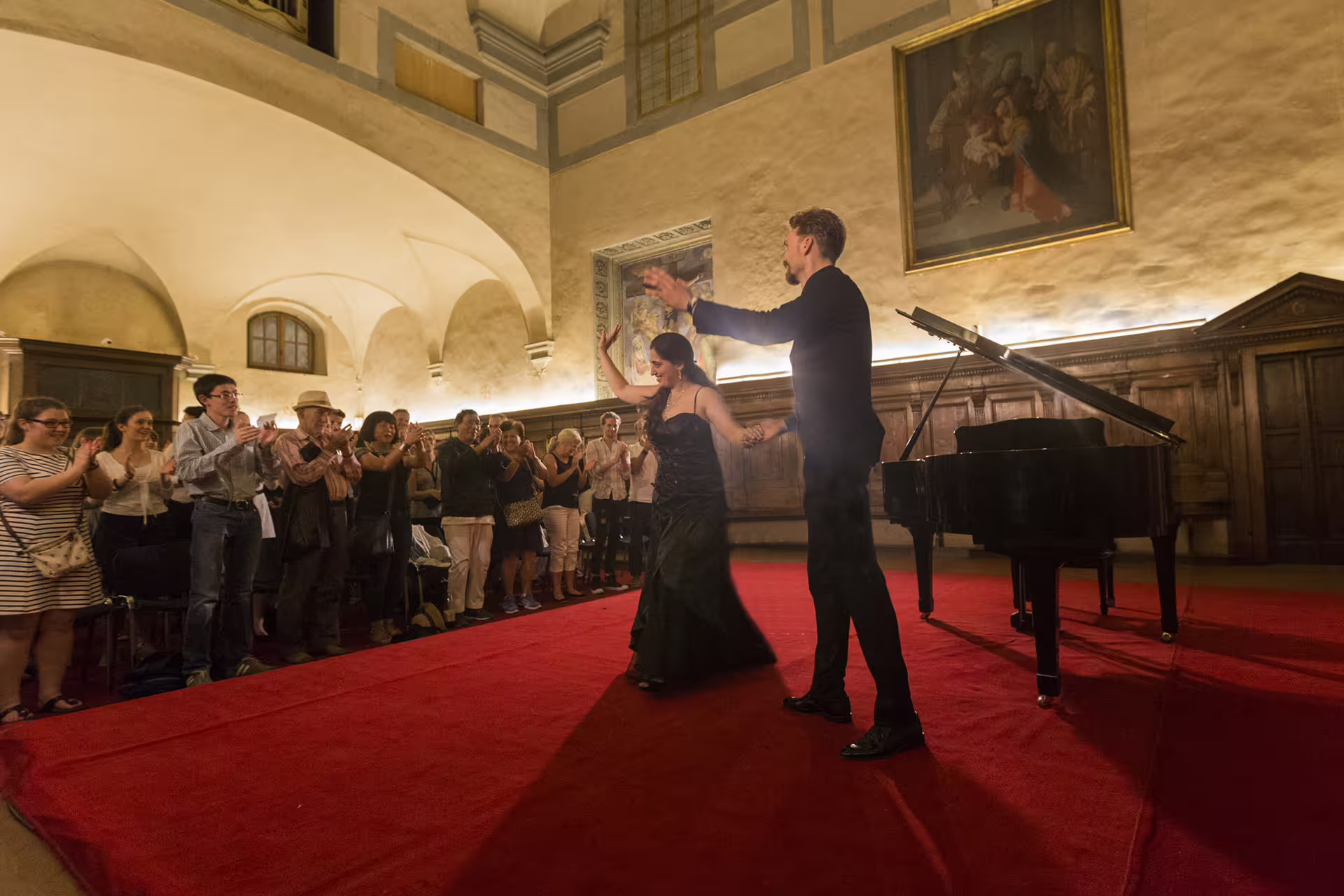 Audience applauds opera singers beside grand piano at Santa Monaca Church Italian opera concert in Florence