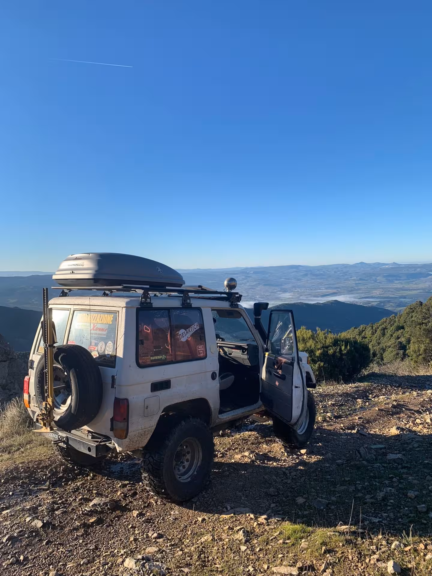 Off-road jeep parked on Mount Limbara with panoramic views of Sardinian landscape under clear blue sky.