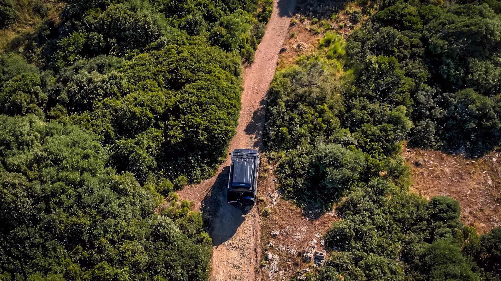 Top-down view of a jeep driving through dense green forest trails in the picturesque landscapes of Iglesias.