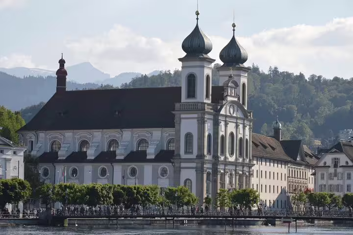 Beautiful Jesuit Church in Lucerne with its baroque architecture, set against a backdrop of lush hills and serene lake.