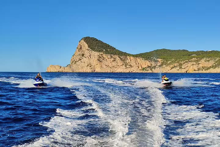 Jet skis speeding across Ibiza sea toward rocky coastline, guided ride to Cala Salada with ocean spray