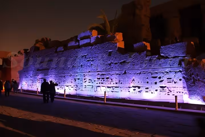 Visitors walking beside purple-lit Karnak Temple walls during Luxor Light and Sound Show with private transfer
