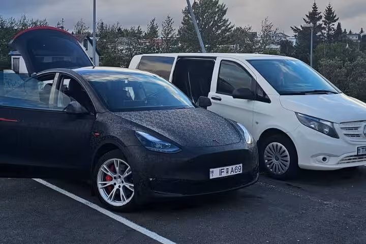 Two vehicles, a black car and a white van, parked for private transfer service between Reykjavik and Keflavik Airport.