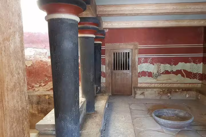 Ancient frescoed room with red and black columns at Knossos Palace, showcasing Minoan architectural elegance.