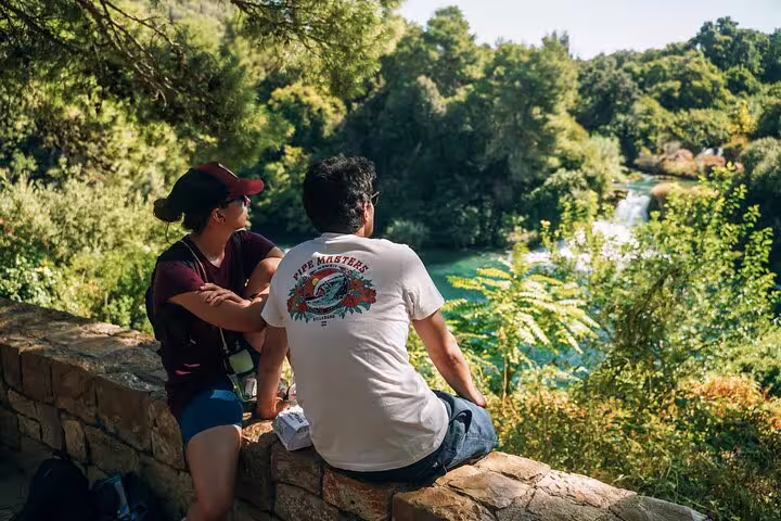 Tourists relaxing at Krka National Park viewpoint overlooking waterfalls on scheduled boat cruise tour