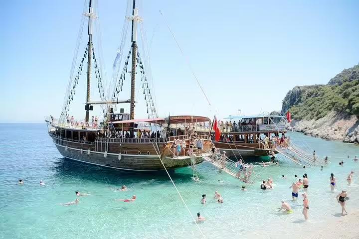 Tourists enjoy swimming near traditional wooden boats docked at a pristine beach on a Kusadasi national park tour.