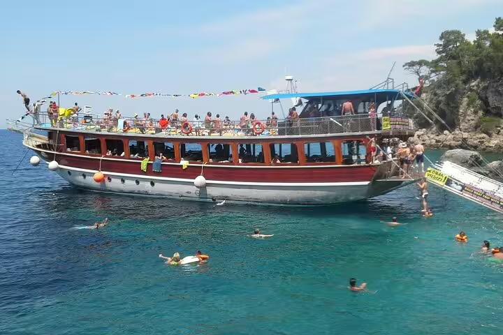 Tourists swimming and relaxing around a traditional boat on a sunny Kusadasi National Park excursion.
