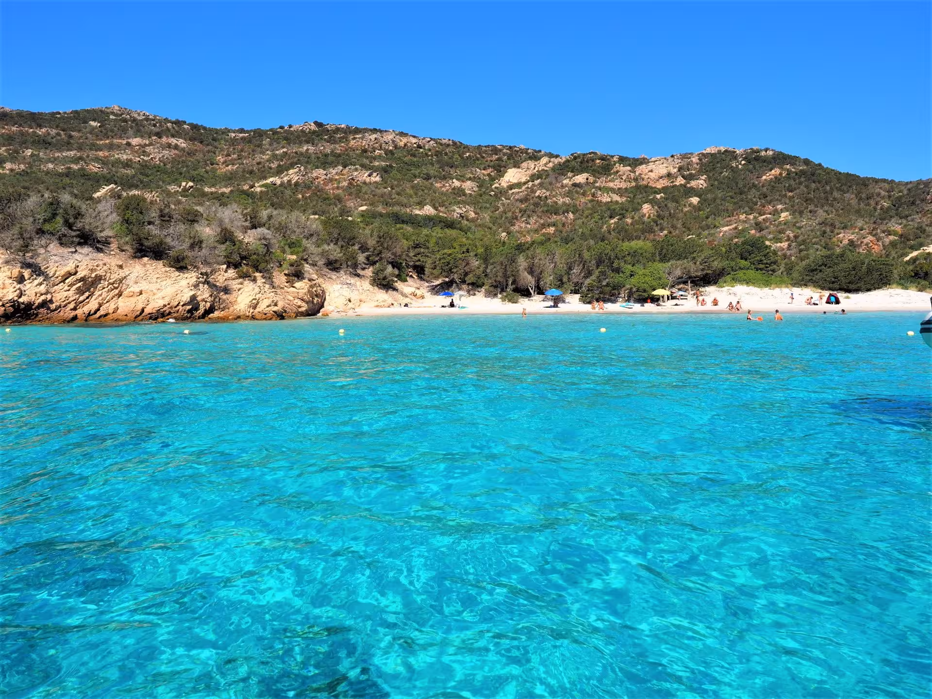 Pristine sandy beach with clear blue waters and distant hills on a La Maddalena dinghy excursion from Palau.