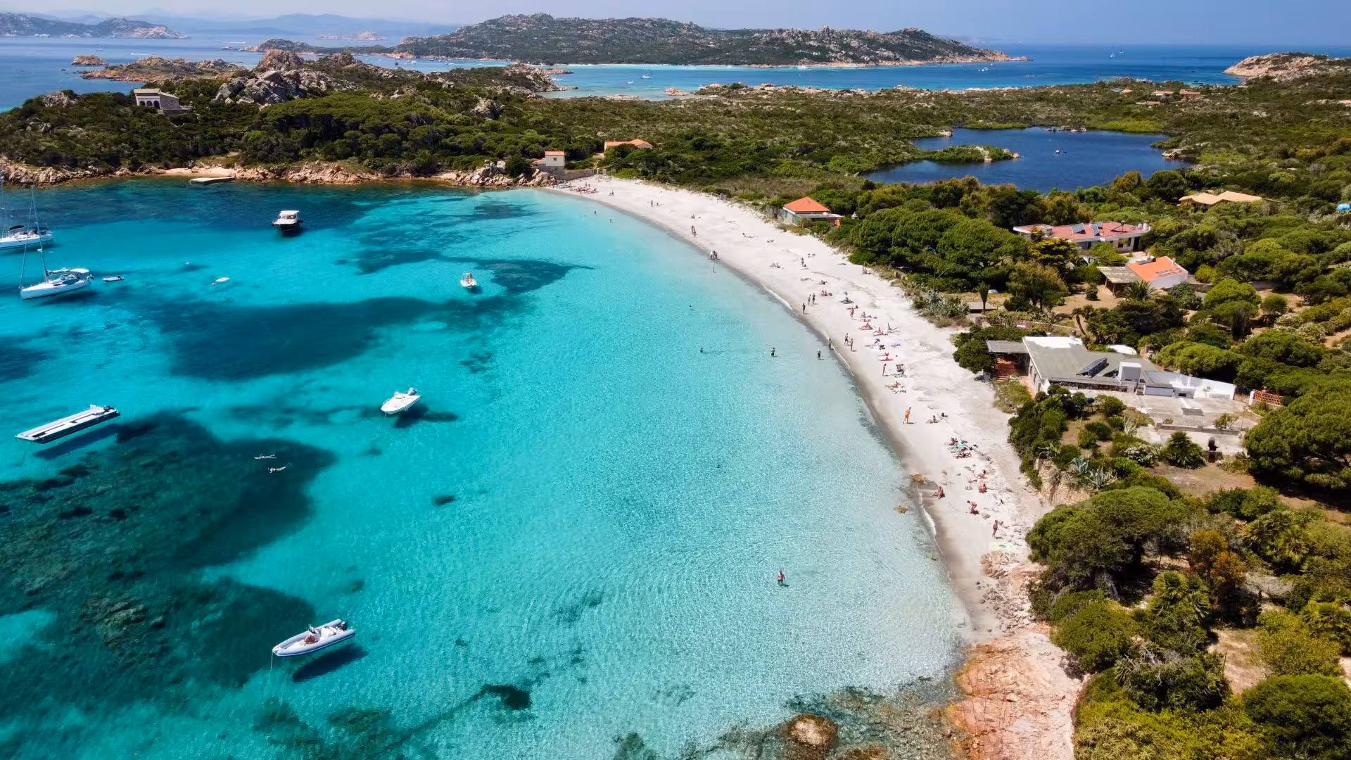 Aerial view of La Maddalena's pristine beach with turquoise water and anchored boats, ideal for a yacht excursion.