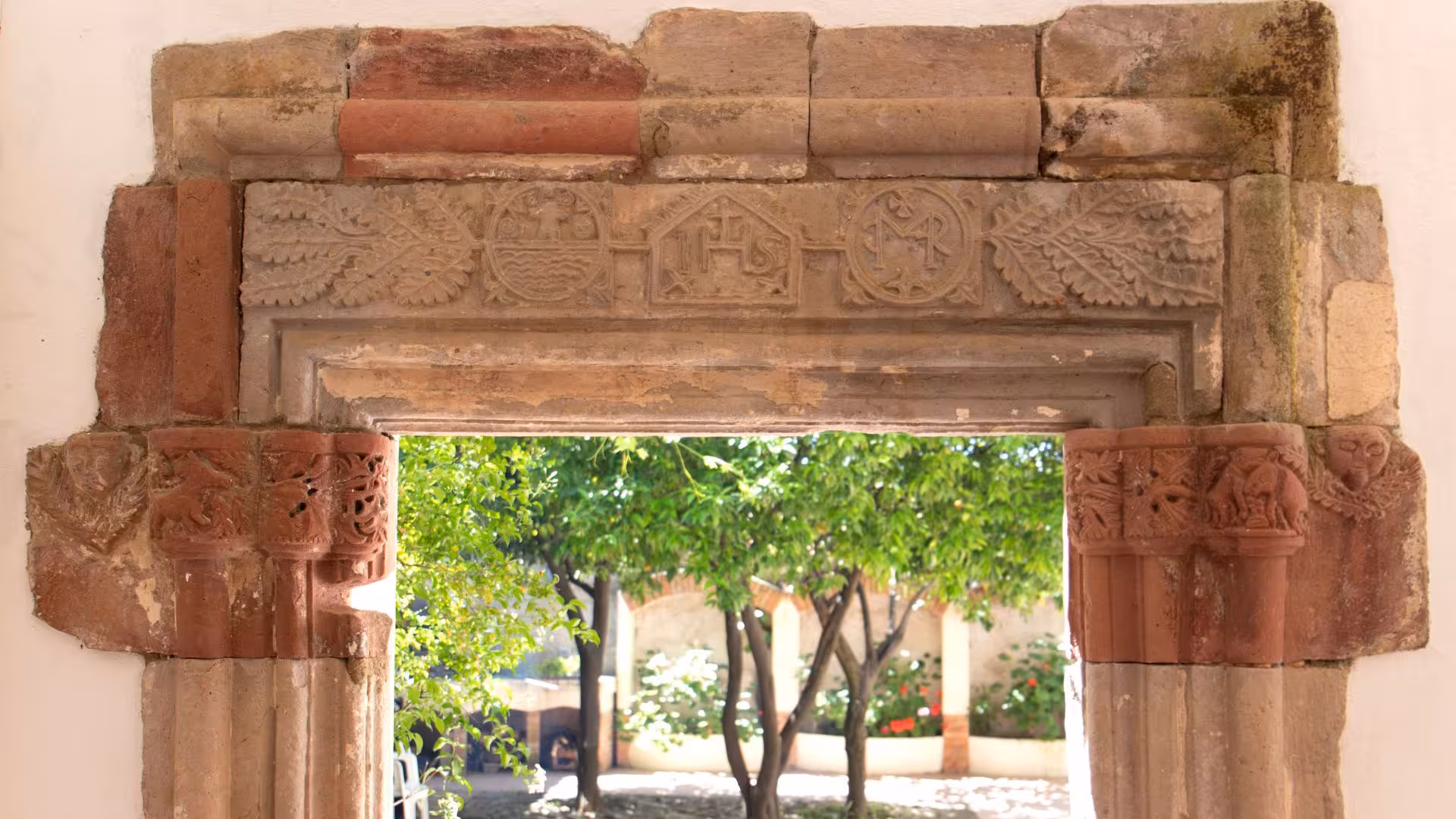 Intricately carved stone doorway frames a lush courtyard, highlighting Laconi's rich cultural heritage.
