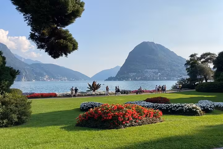 Lake Lugano waterfront park with colorful flowerbeds and mountains on guided tour from Como to Bellagio