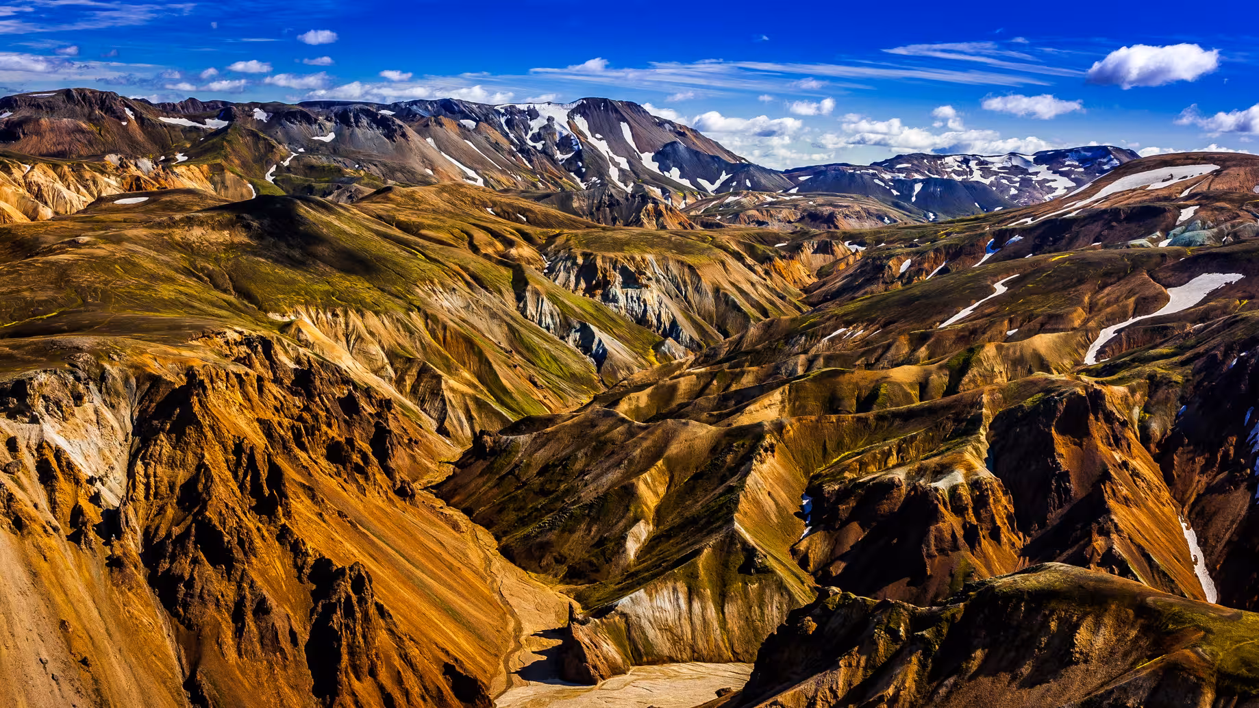 Aerial view of Landmannalaugar's vibrant, multicolored mountains and valleys under a clear blue sky.