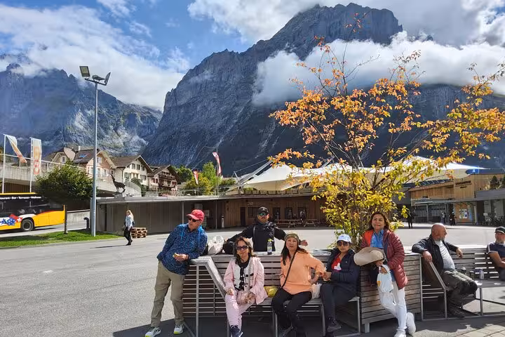 Travelers relaxing in Lauterbrunnen village with dramatic Jungfrau peaks and autumn tree on 4-day Swiss Alps tour