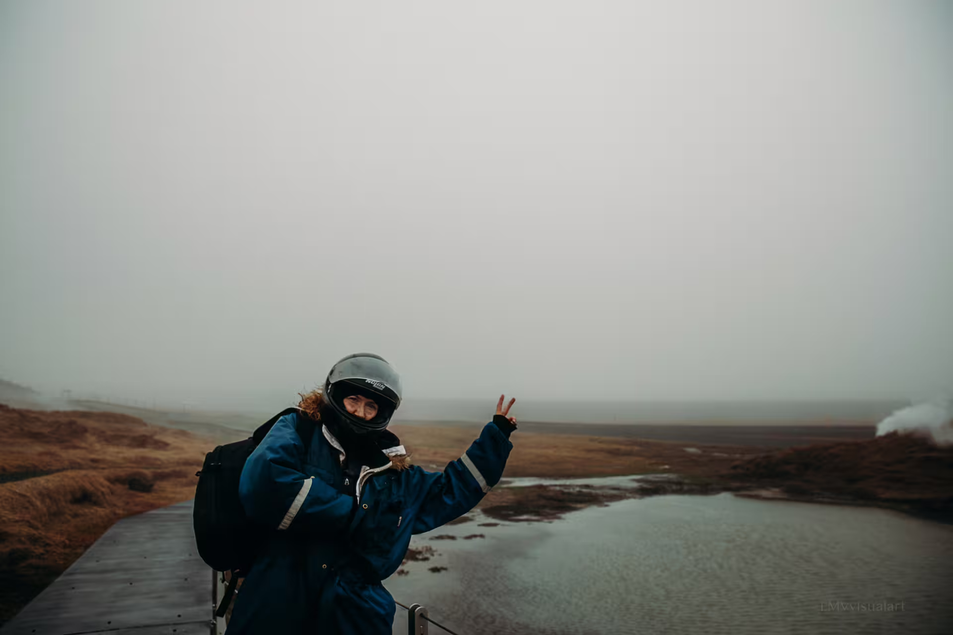 Adventurer in helmet and gear flashes peace sign on rugged lava field buggy tour with misty, scenic volcanic landscape backdrop.