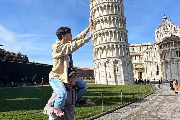 Tourists creatively pose with the Leaning Tower of Pisa on a sunny day during a Tuscany small group tour.