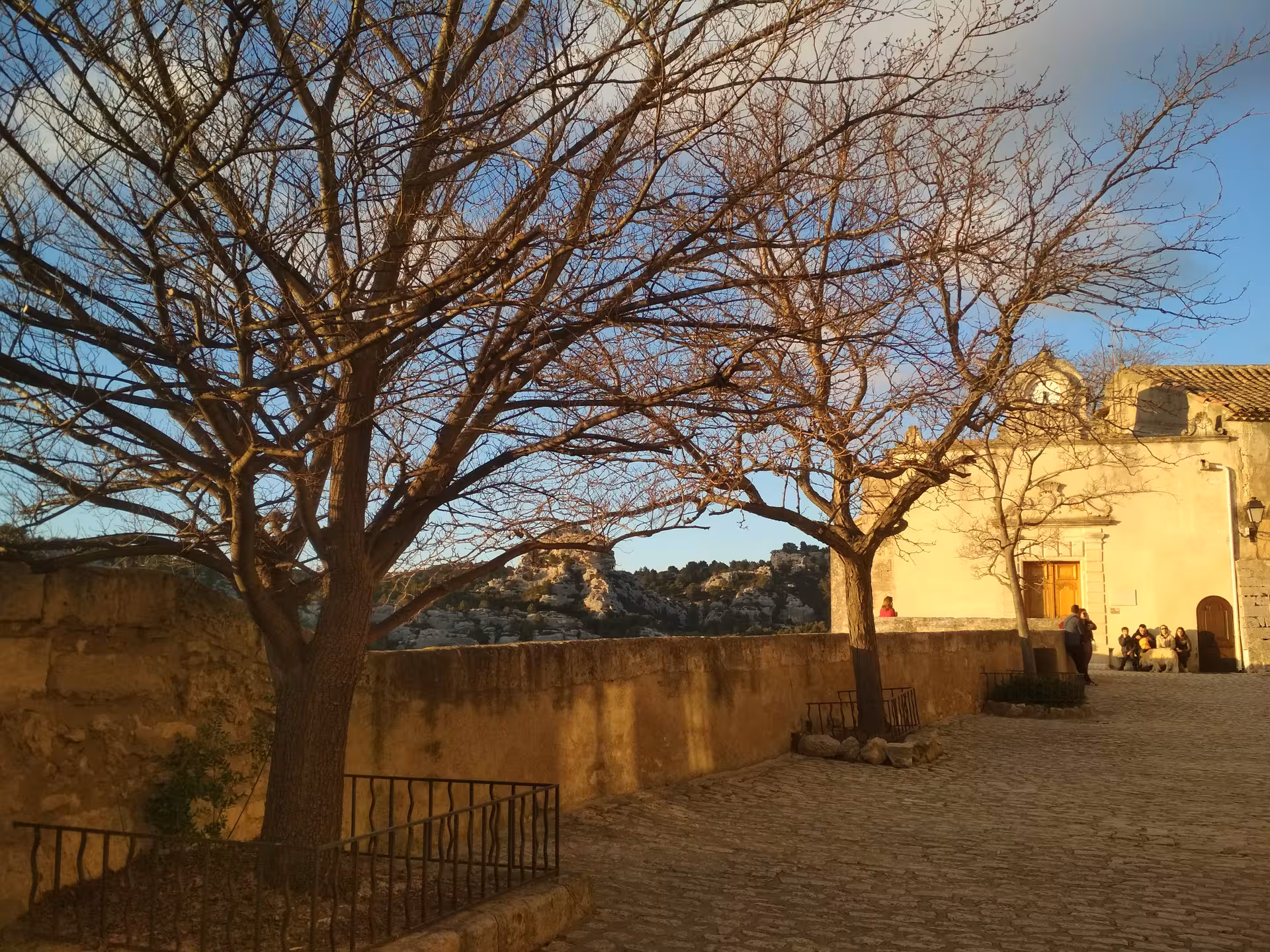 Leafless trees and chapel plaza in Les Baux-de-Provence at sunset, Alpilles panorama on Provence day trip