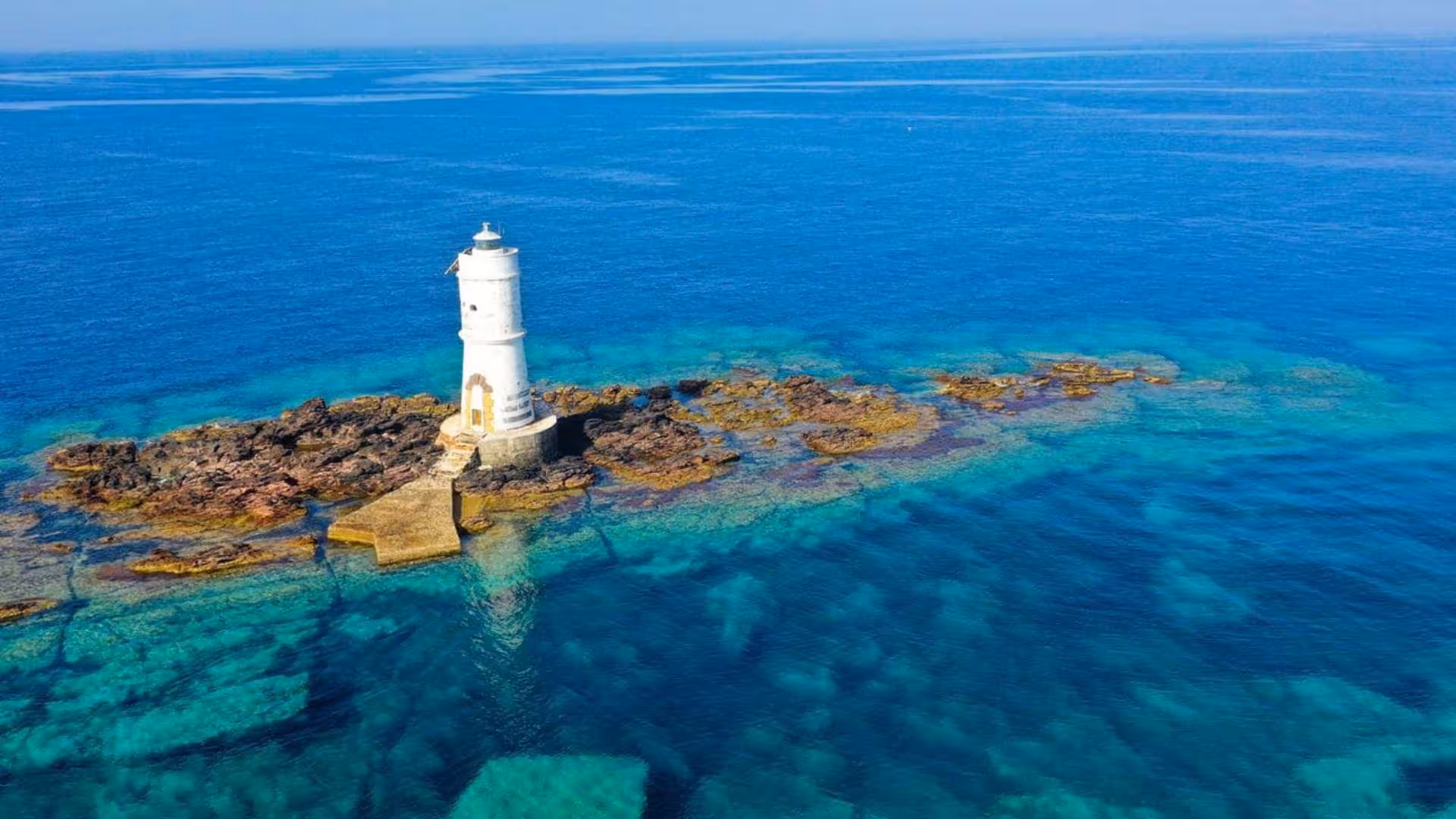 Iconic lighthouse on rocky islet surrounded by azure waters, seen on a dinghy tour between Carloforte and Sant'Antioco.