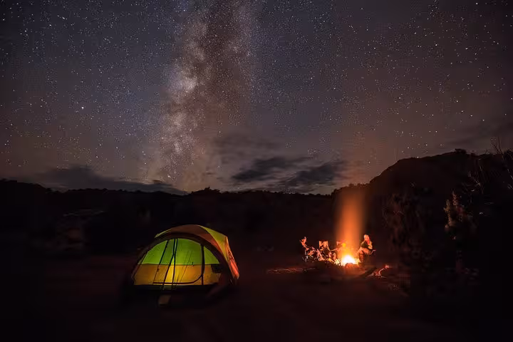 Milky Way over desert campsite with glowing tent and campfire, ideal for a private Liwa overnight safari under the stars.
