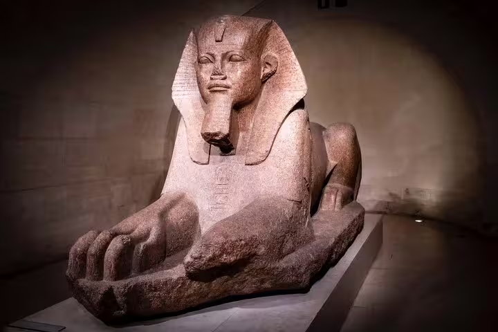 Ancient Sphinx statue on display in the Louvre Museum's Egyptian Antiquities section during a guided tour.