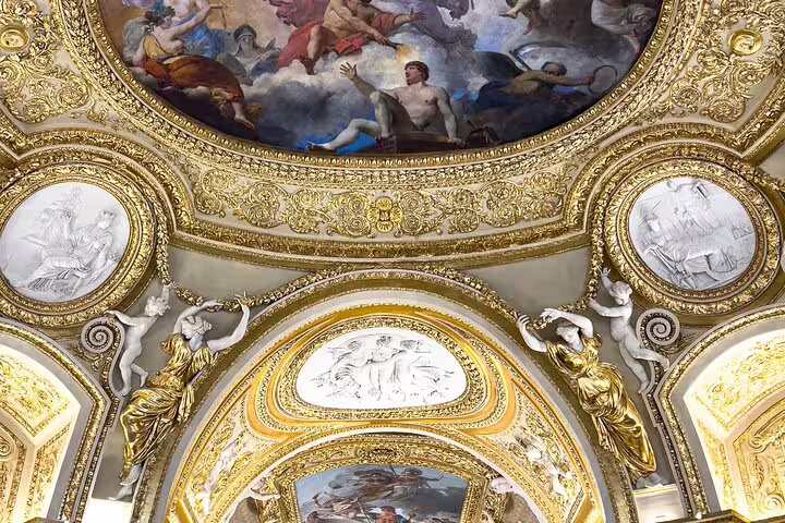 Intricate ceiling artwork in a gallery at the Louvre Museum, showcasing opulent gold detailing and classical paintings.