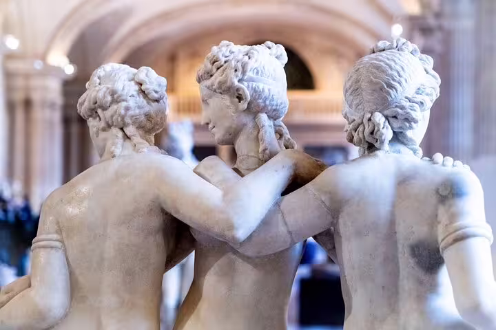 Close-up of a classic marble sculpture of three figures inside the Louvre Museum, highlighting artistic elegance.