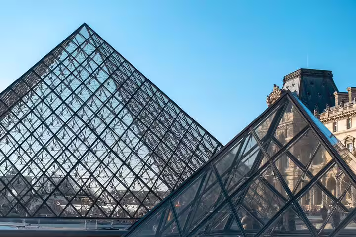 The iconic glass pyramid entrance of the Louvre Museum against a clear blue sky, showcasing architectural elegance.