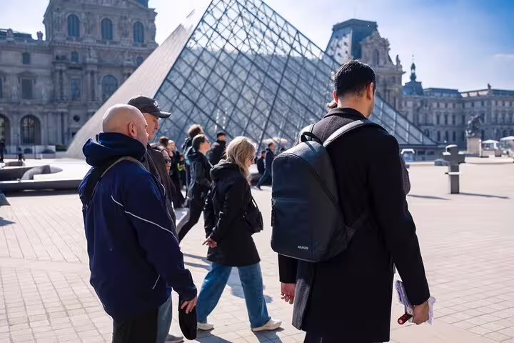 Tourists exploring the iconic glass pyramid entrance of the Louvre Museum on a sunny day.