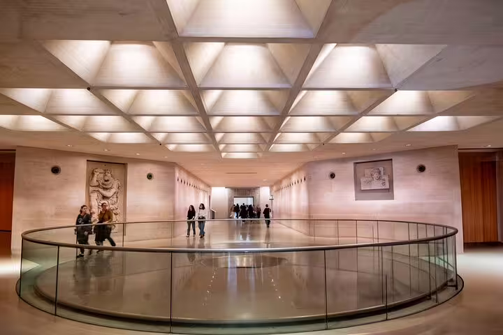 Visitors walking through the modern architecture of the Louvre Museum's entrance hall during a guided tour.