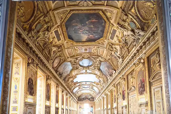 Elaborate hallway interior of the Louvre Museum featuring ornate ceilings adorned with rich frescoes and carvings.