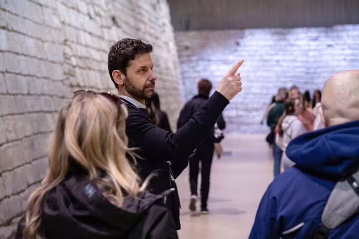 Tour guide leading a group through the historic stone walls of the Louvre Museum, pointing out key details.