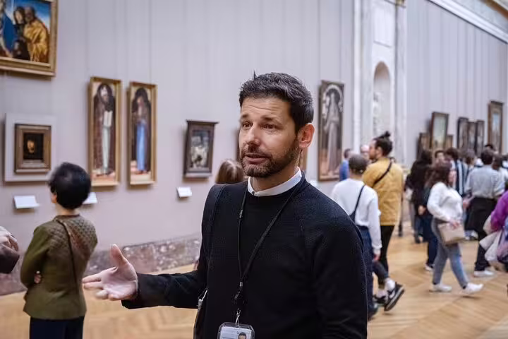 Engaged tour guide explaining artworks to visitors in the Louvre Museum's gallery corridor.