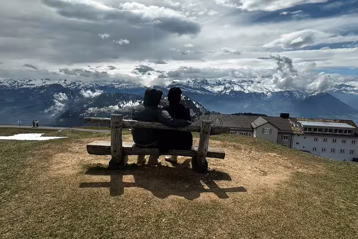 Two people sitting on a bench with stunning views of the snowy Swiss Alps from Mount Rigi.
