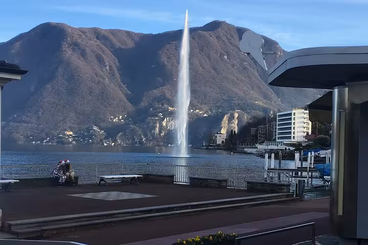 Lugano waterfront promenade with tall lake fountain and Alps backdrop, highlight of Milan to Como Bellagio cruise