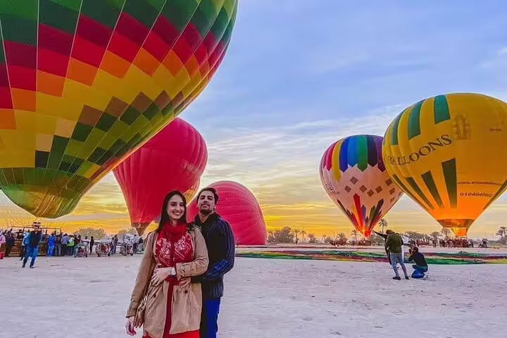 Couple posing at Luxor hot air balloon launch site at sunrise with colorful balloons ready for flight, Egypt