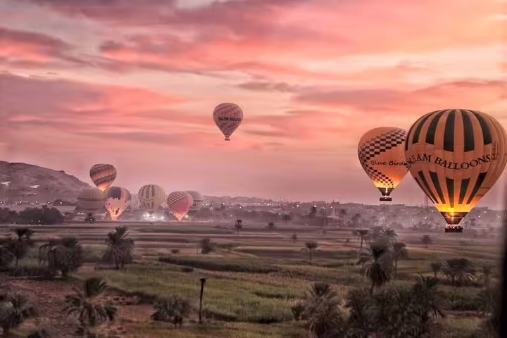 Multiple hot air balloons drifting over Luxor farmland at dawn, scenic sunrise flight above the Nile Valley