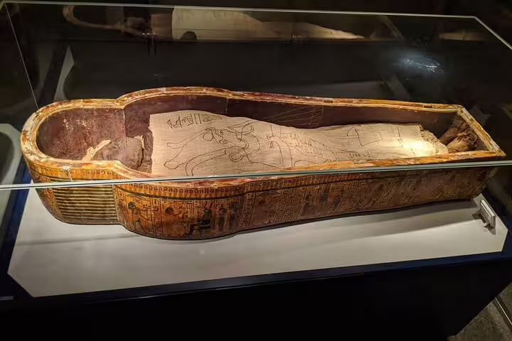 Decorated wooden coffin with hieroglyphs in glass case at Luxor Museum, half-day Luxor museum tour