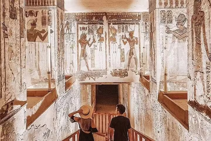 Travelers descending into a Luxor tomb with wall art, on private Cairo to Luxor sleeper train trip