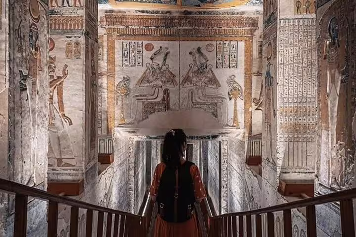 Traveler descending into an ancient Luxor tomb with hieroglyph walls on private Cairo to Luxor sleeper train tour