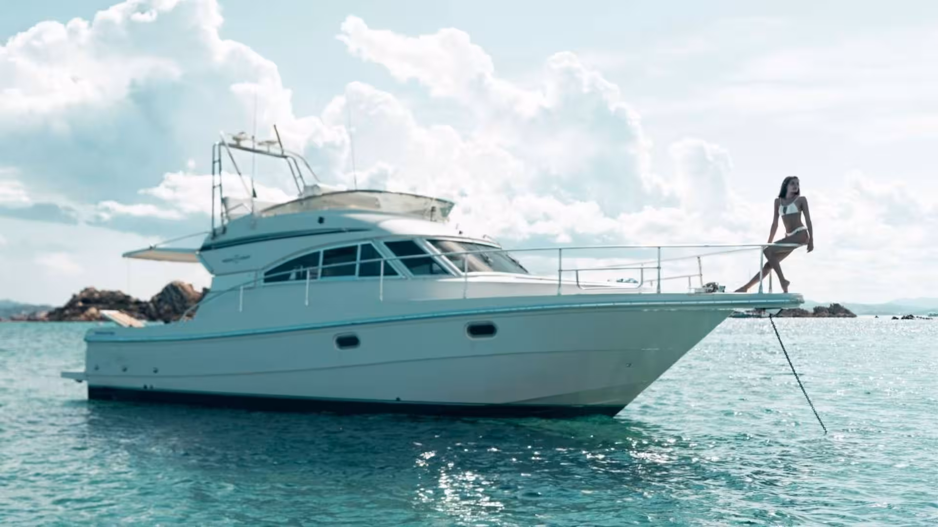 Luxurious mini yacht anchored in La Maddalena, woman enjoying serene views on a sunny day.