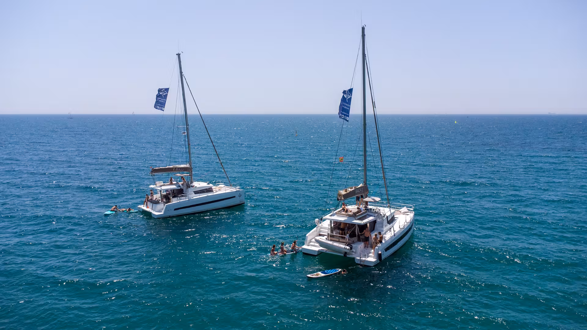 Two Bali 4.2 luxury catamarans off Barcelona with guests swimming and paddleboarding on a 4-hour private cruise
