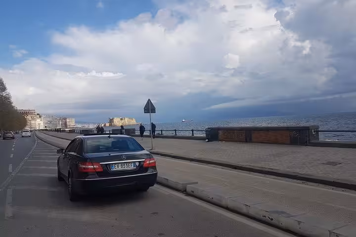 Luxury Mercedes parked along Naples seaside, offering private transfer from Sorrento to Naples hotel or airport.