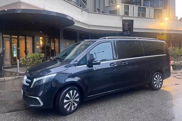 Luxury black van ready for private transfer from Milan to Interlaken, parked outside a modern hotel entrance.
