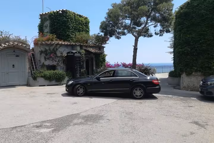 Luxury sedan parked by a scenic villa with ocean views, ideal for private transfers from Sorrento to Naples.