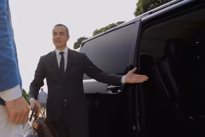 Chauffeur in a suit opens a luxury vehicle door, providing professional transfer service from Cortina to Venice.