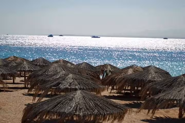 Mahmya Island beach straw umbrellas and sparkling Red Sea, full-day snorkeling sea trip from Hurghada