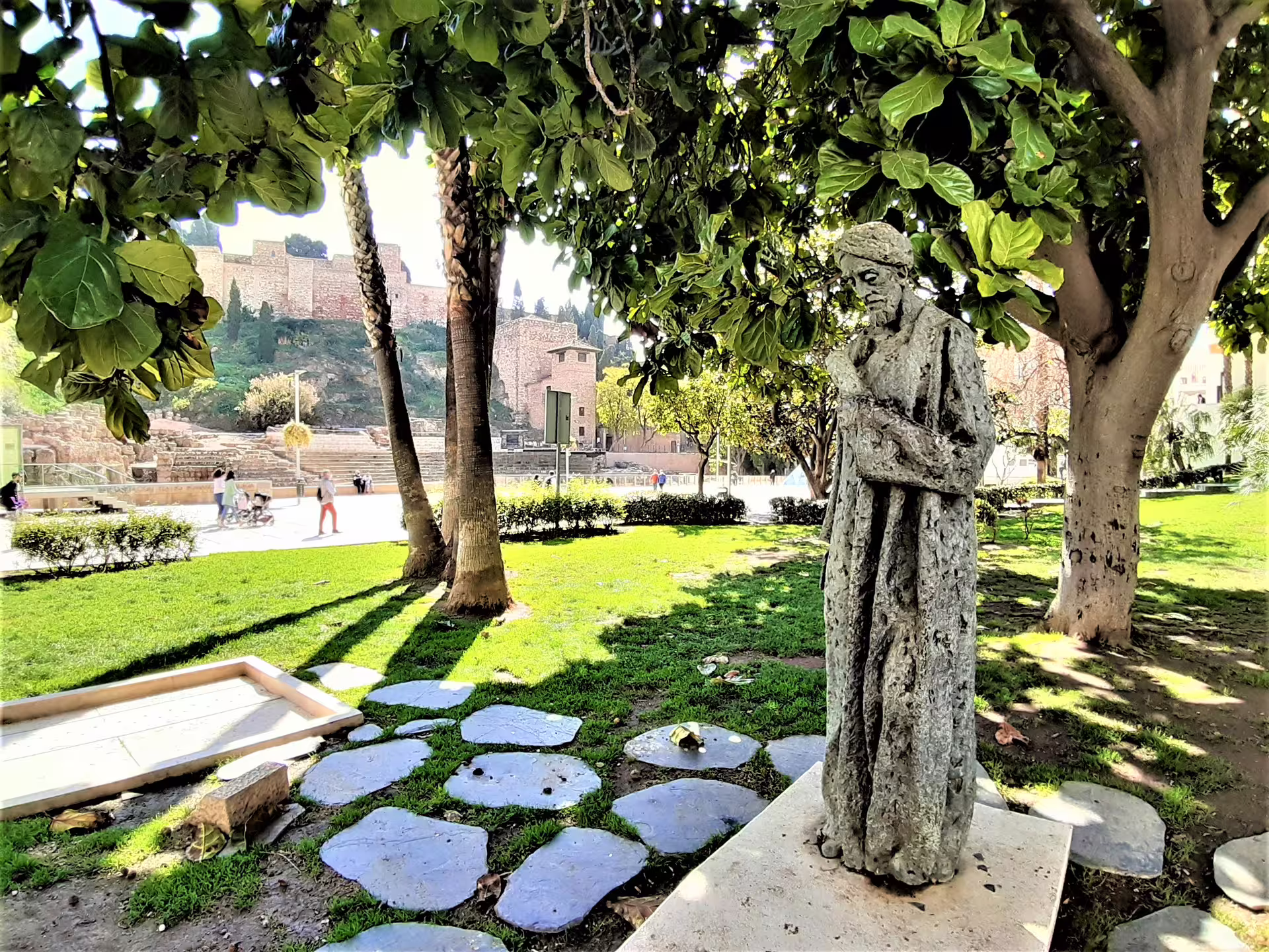 Stone statue in Malaga park with Alcazaba fortress views, featured on a private full-day tour with hotel pick-up