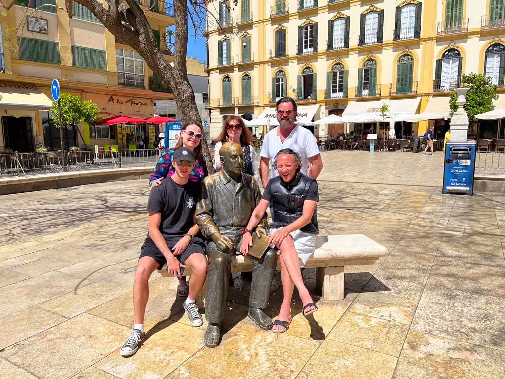 Travelers posing by a bronze bench statue in Malaga plaza on a private full-day city tour with hotel pick-up