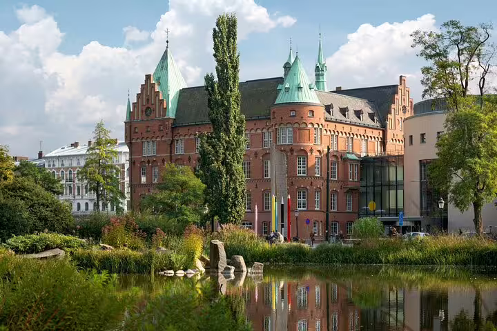 Historic building with green copper spires reflecting in a serene pond in Malmö, featured on a full-day train tour from Copenhagen.