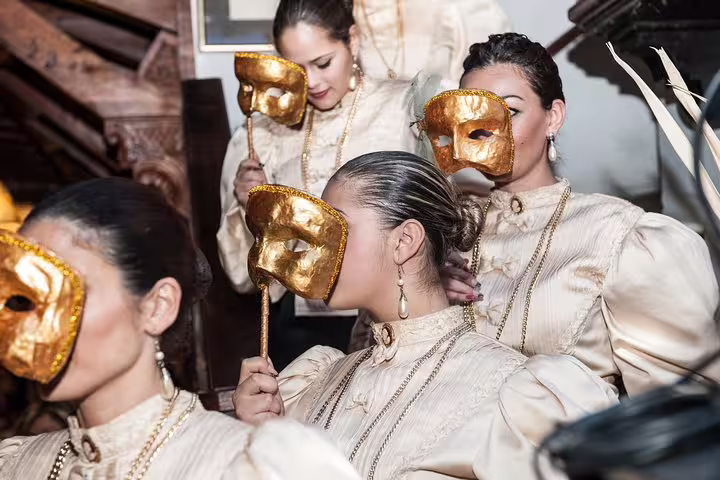 Women in elegant costumes hold golden masks at the Maltese Folklore Night Tour, highlighting traditional Maltese culture.